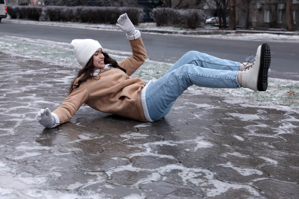 Young woman fallen on slippery icy pavement outdoors.