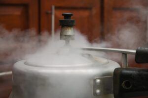 Steam escaping from lid of pressure cooker with reflection of modern kitchen.