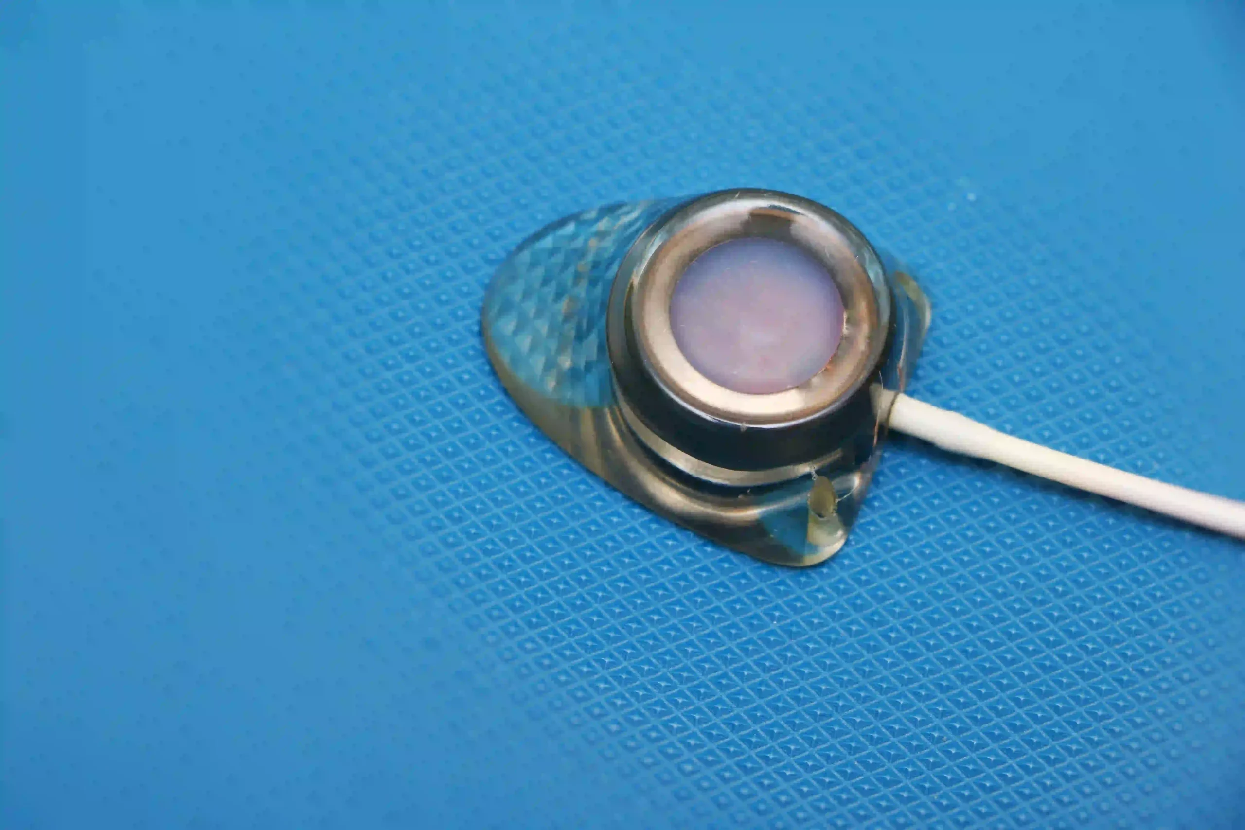 Close-up of a stethoscope earpiece with gel residue on a blue surface