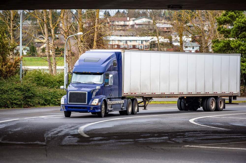 Blue 18-wheeler truck passing under the bridge.