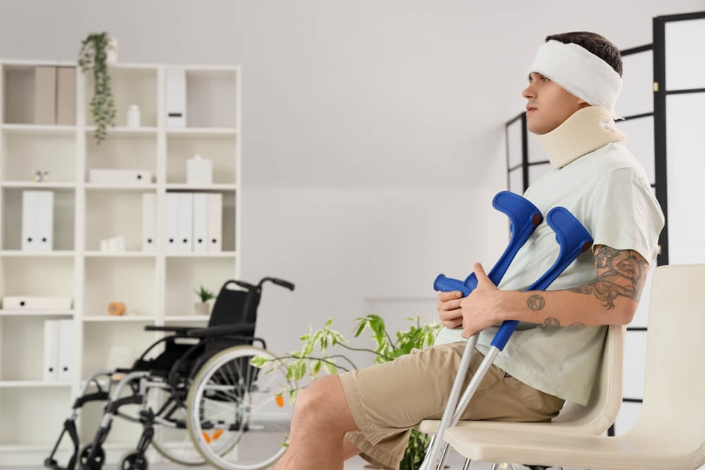 Injured man sitting with head bandage and crutches.