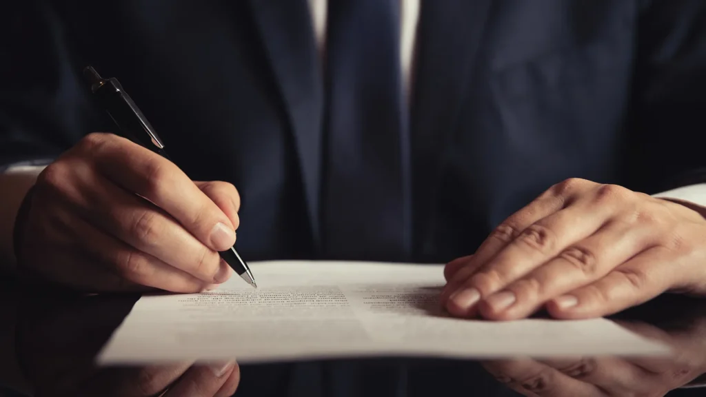  A man in a suit is signing a document, demonstrating professionalism and attention to detail.
