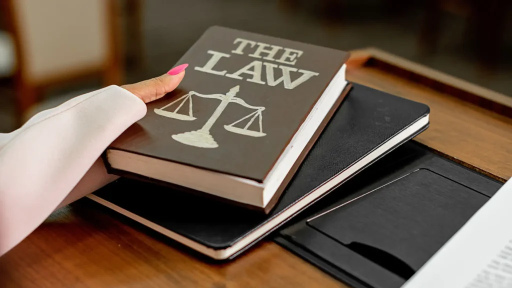 Hand holding a 'The Law' book on a table with documents.