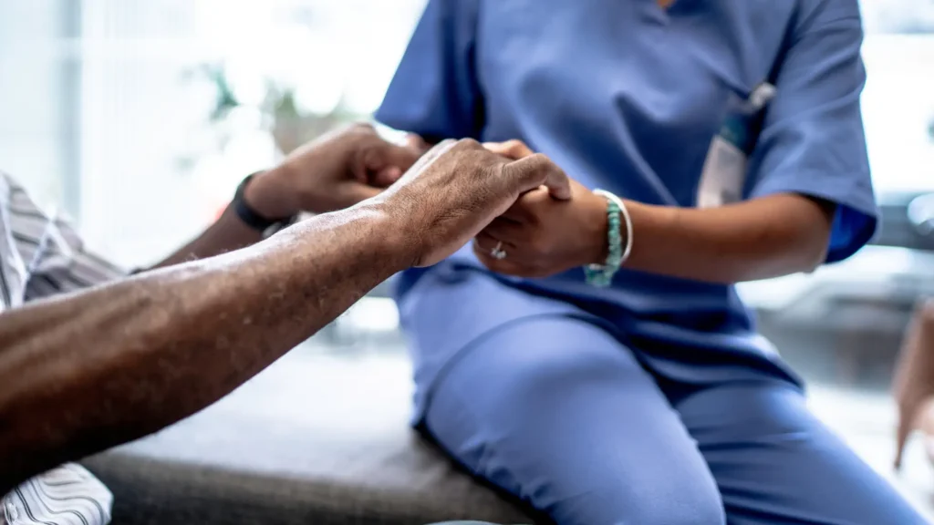 Caregiver in blue scrubs holding hands with an elderly patient