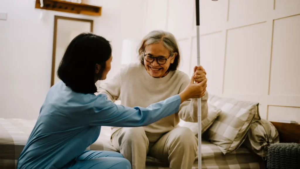 Caregiver assisting a smiling elderly woman using a white cane